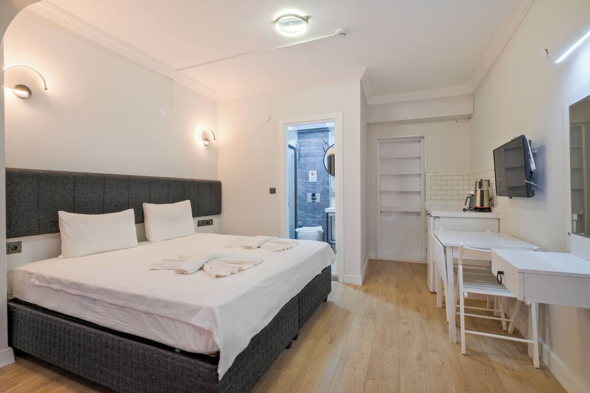 Un dormitorio con cama, mesitas de noche, un espejo y un baño visible a través de una puerta abierta.
