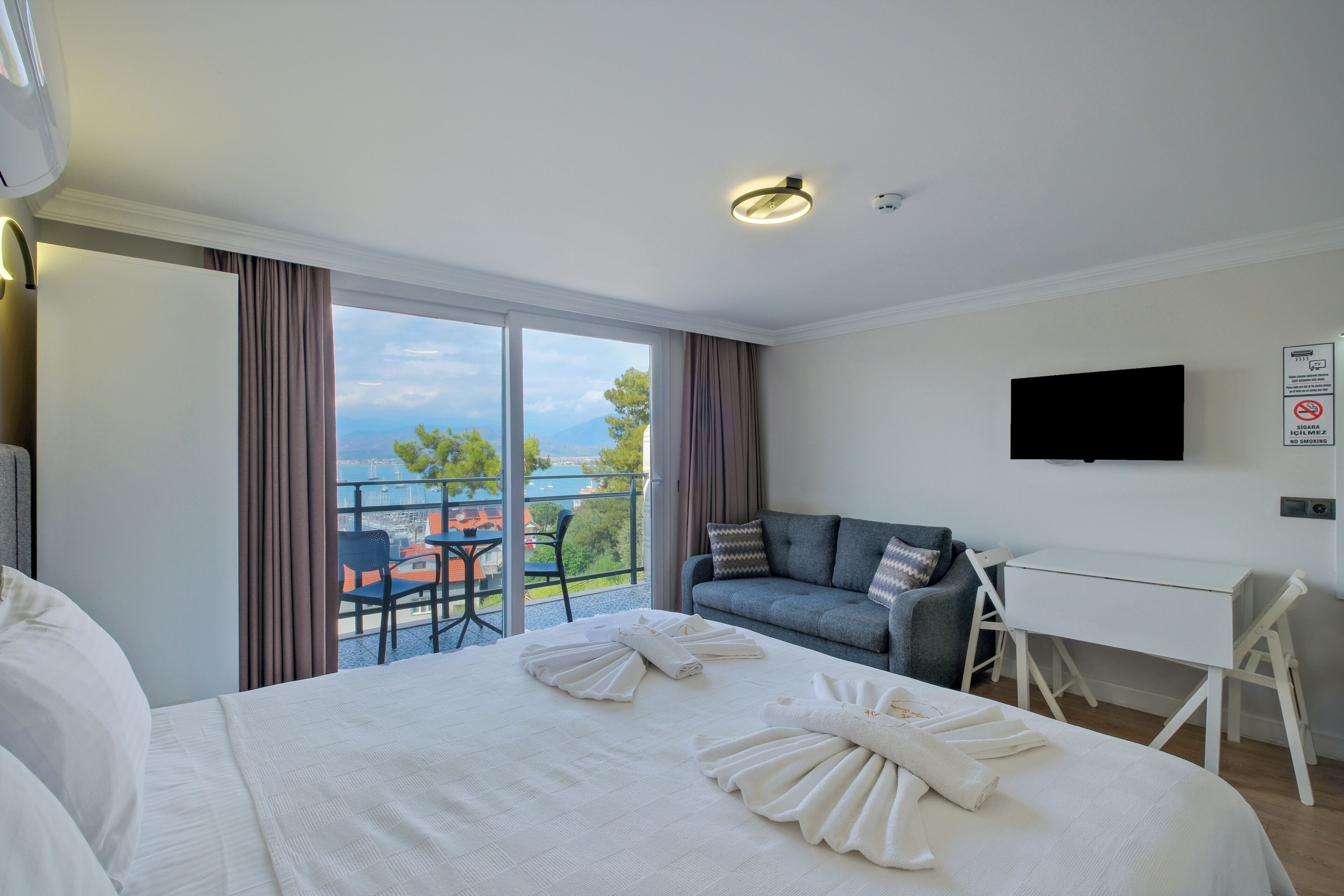 Una habitación de hotel con cama, escritorio, televisor y balcón con vistas.