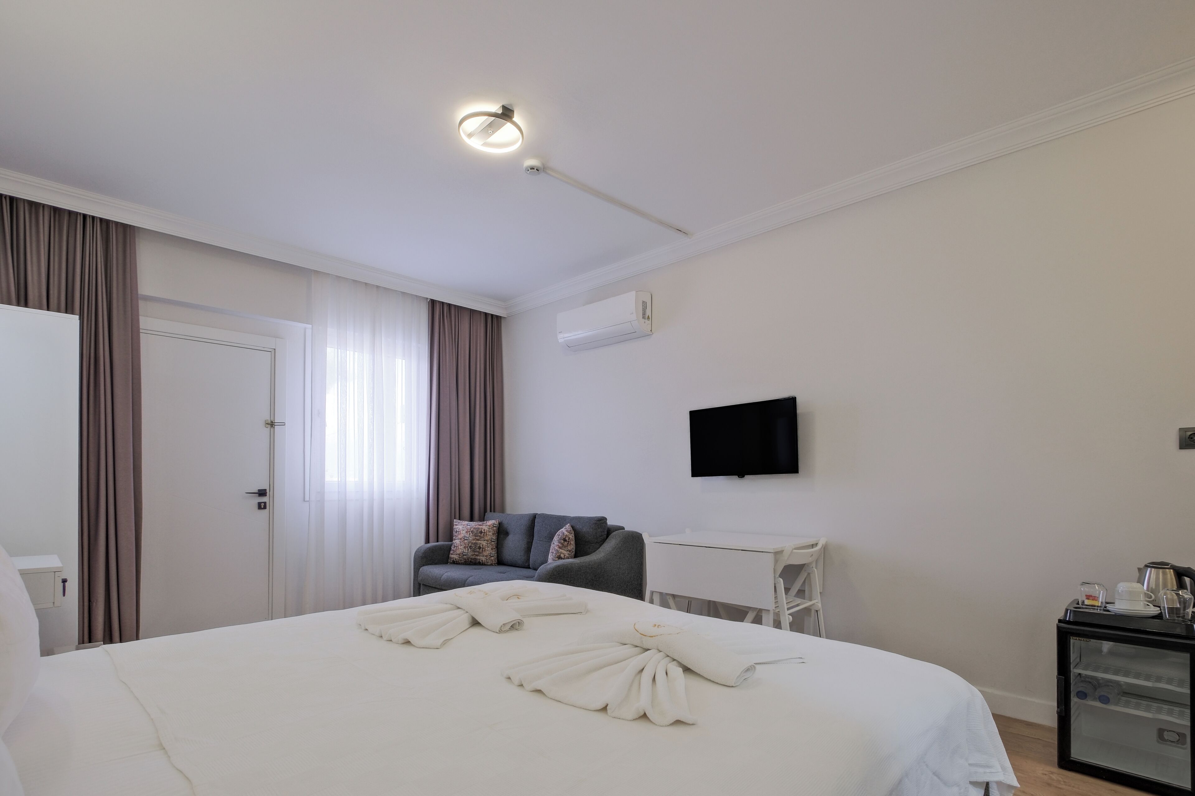 A hotel room with a bed, a desk, a chair, a television, and an air conditioning unit.