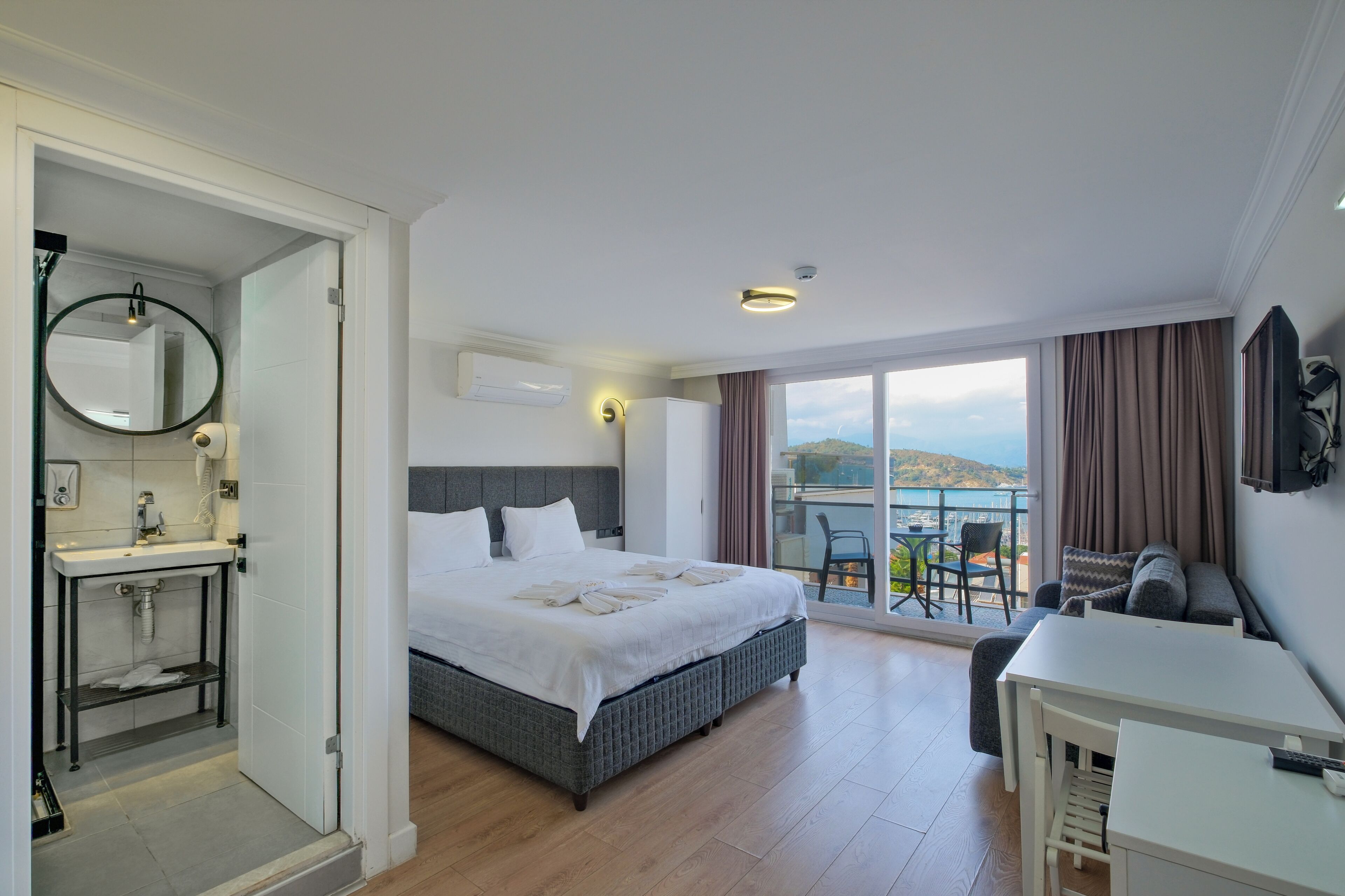 A hotel room with a bed, a desk, a bathroom, and a balcony with a view.