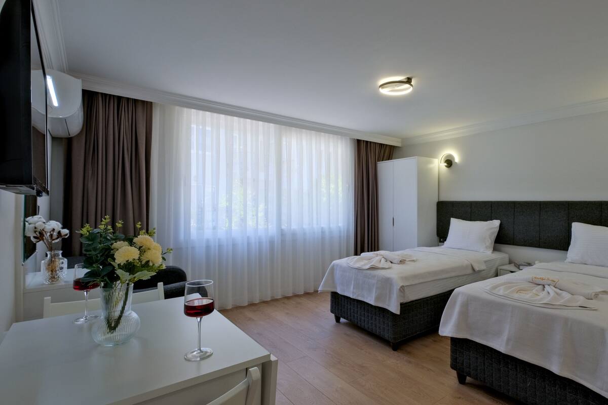 Una habitación de hotel con dos camas, un escritorio y un florero con flores.