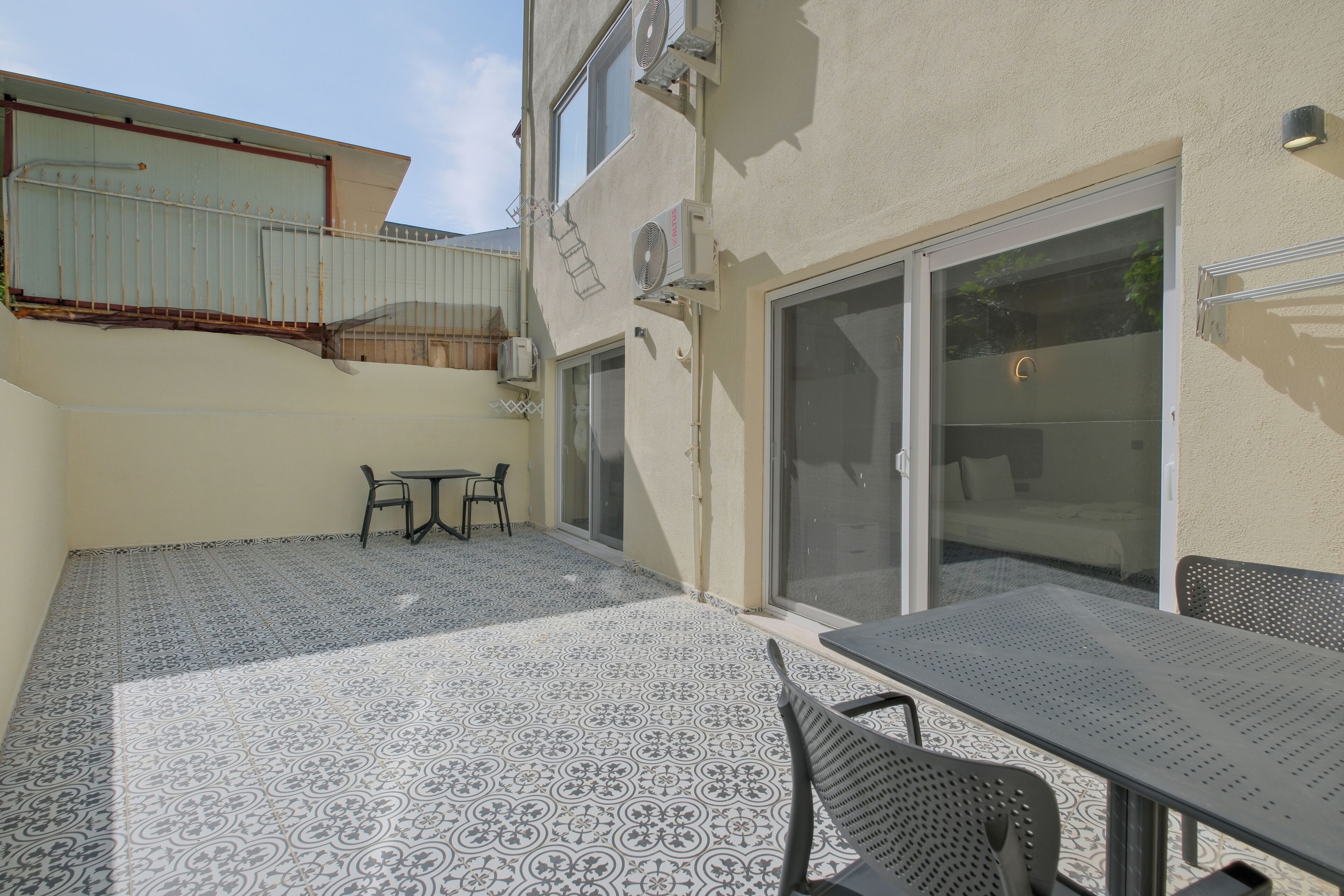 A patio with patterned tiles, a table, chairs, and a sliding glass door leading to an interior space.