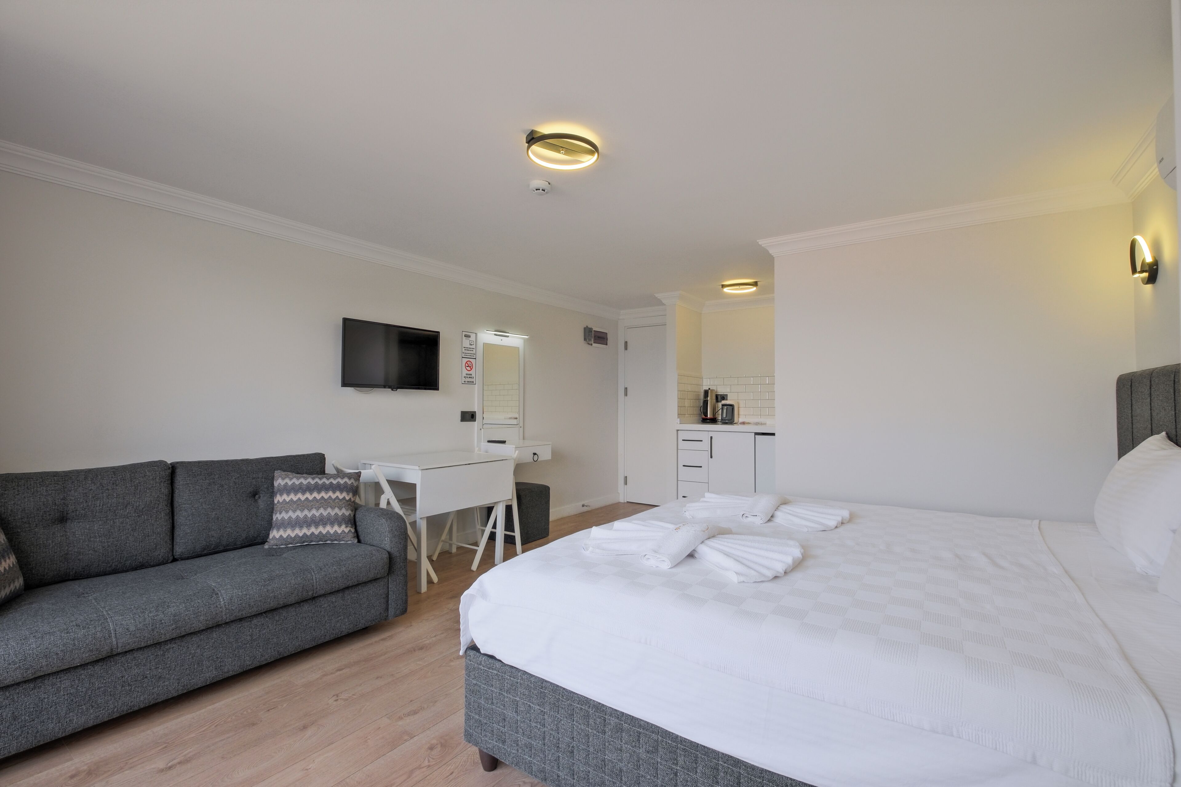 A hotel room with a bed, a sofa, a desk, a mirror, and a kitchenette.