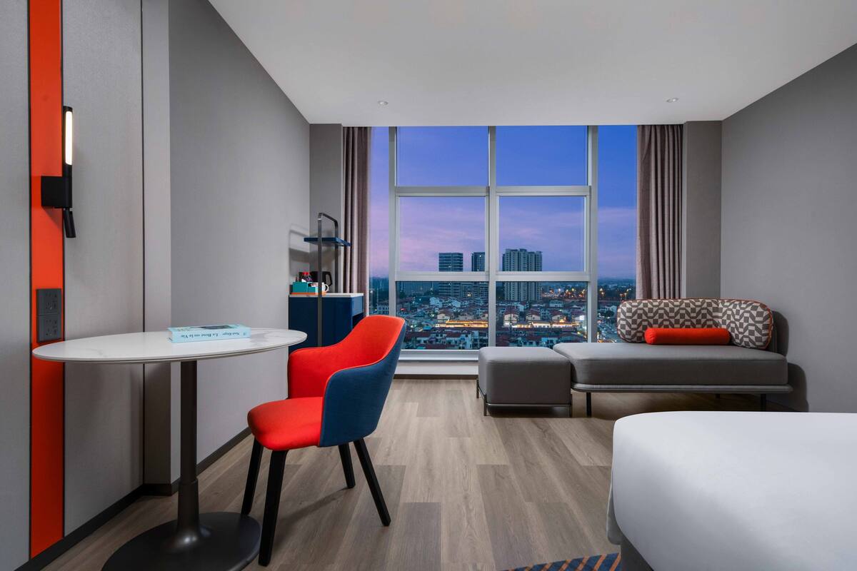 Ein Hotelzimmer mit großem Fenster, Schreibtisch, Sessel, Sofa und Bett.