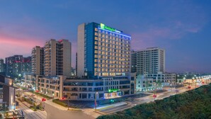 Een Holiday Inn Express hotel met een modern design, omringd door andere gebouwen en een verlichte straat in de schemering.