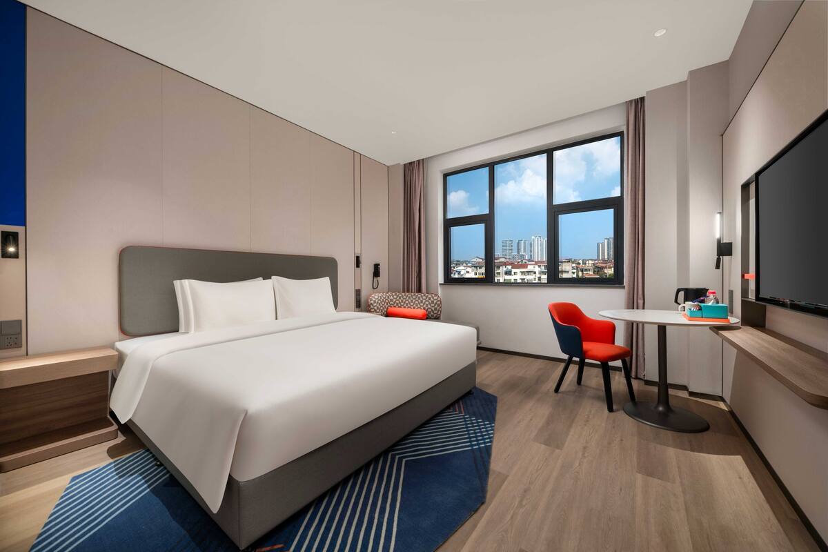 Ein modernes Hotelzimmer mit einem großen Bett, einem Schreibtisch, einem Sessel und einem Fernseher.