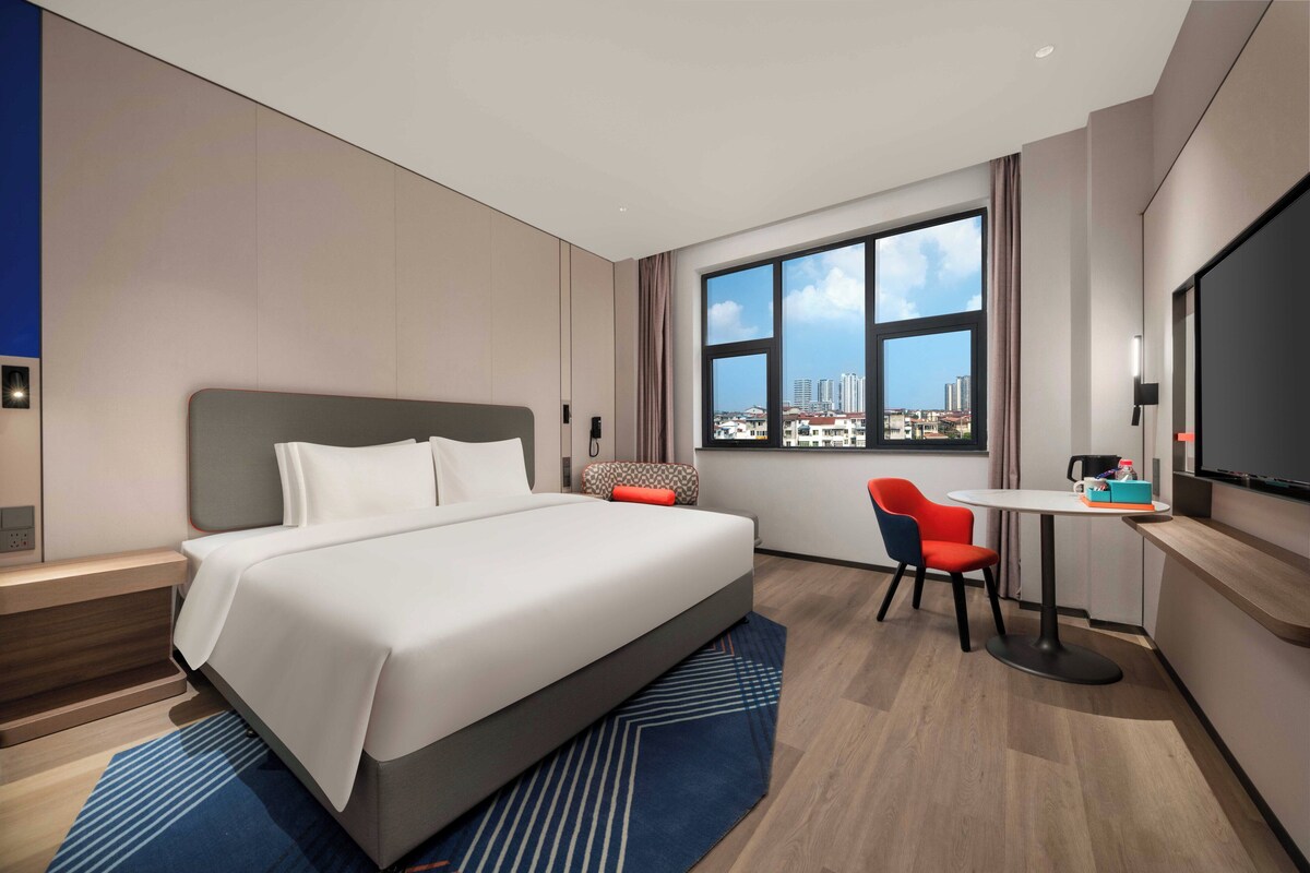 A modern hotel room with a large bed, a desk, a chair, and a TV.