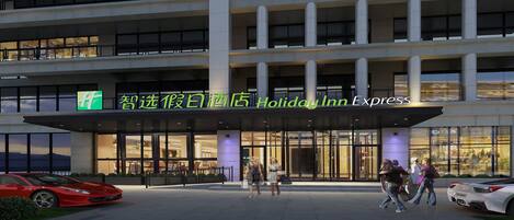 A Holiday Inn Express hotel entrance with a modern design, large windows, and a visible parking area with cars.