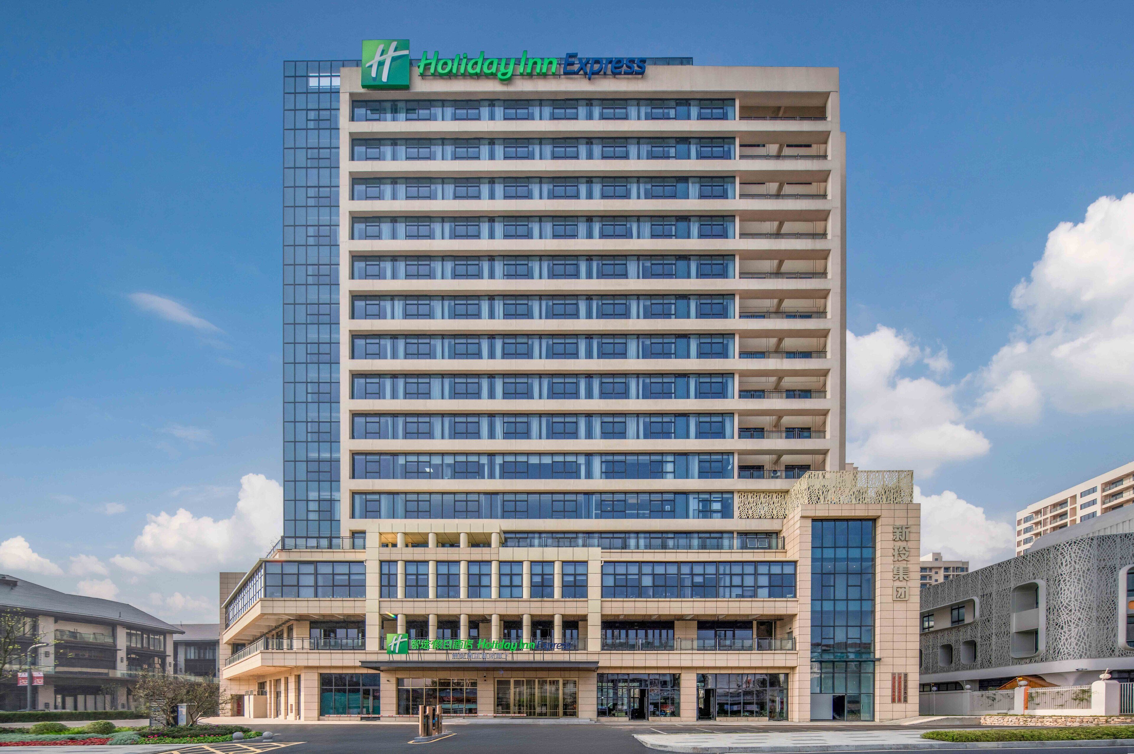 A Holiday Inn Express building with a modern glass facade, multiple floors, and a prominent entrance with a green sign.