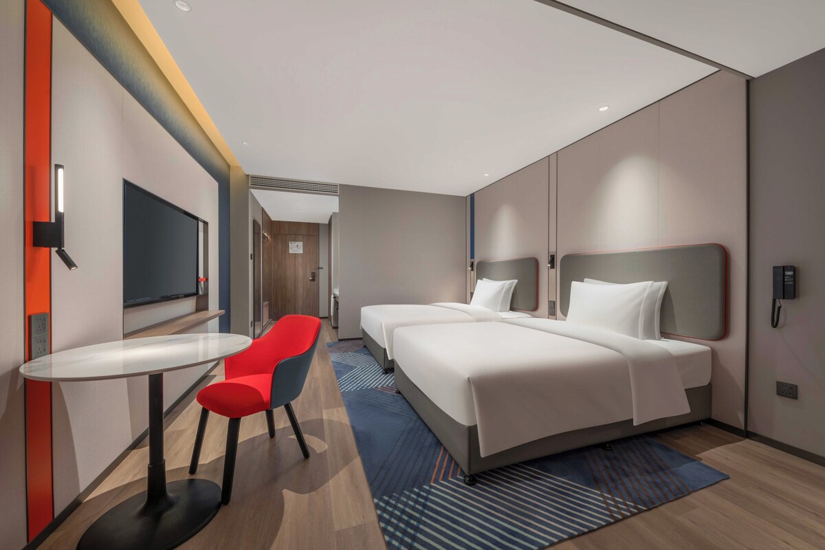 A modern hotel room with a large bed, a small table, and a red chair.