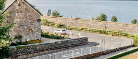 A stone building with a fenced area and a view of a body of water and distant hills.