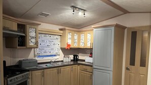 Eine Küche mit Holzschränken, einem Herd, einem Backofen, einem Kühlschrank und einem Fenster mit Blick auf Bäume.
