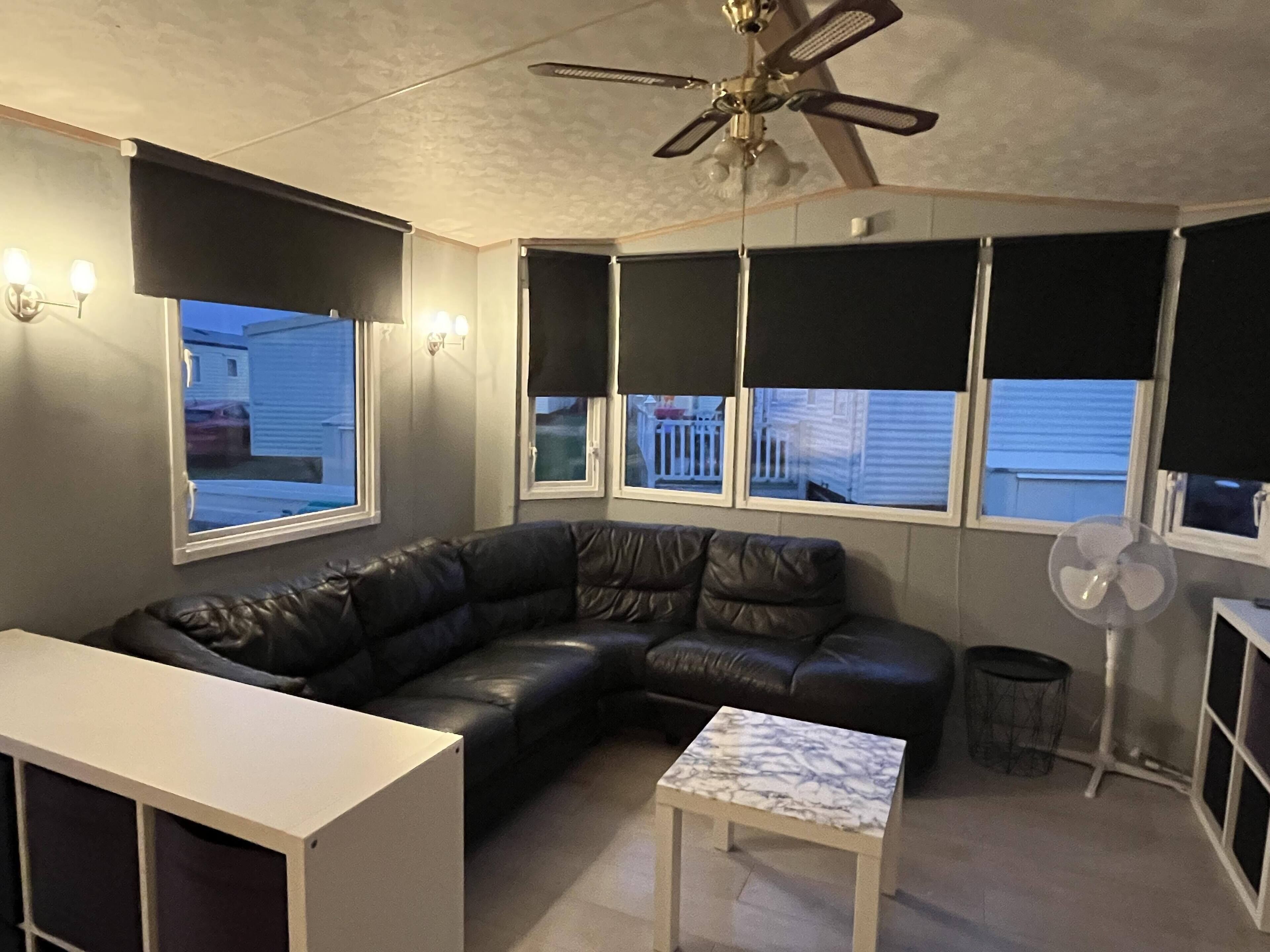 A living room with a black leather sofa, a white coffee table, a ceiling fan, and a window with a view of a house.