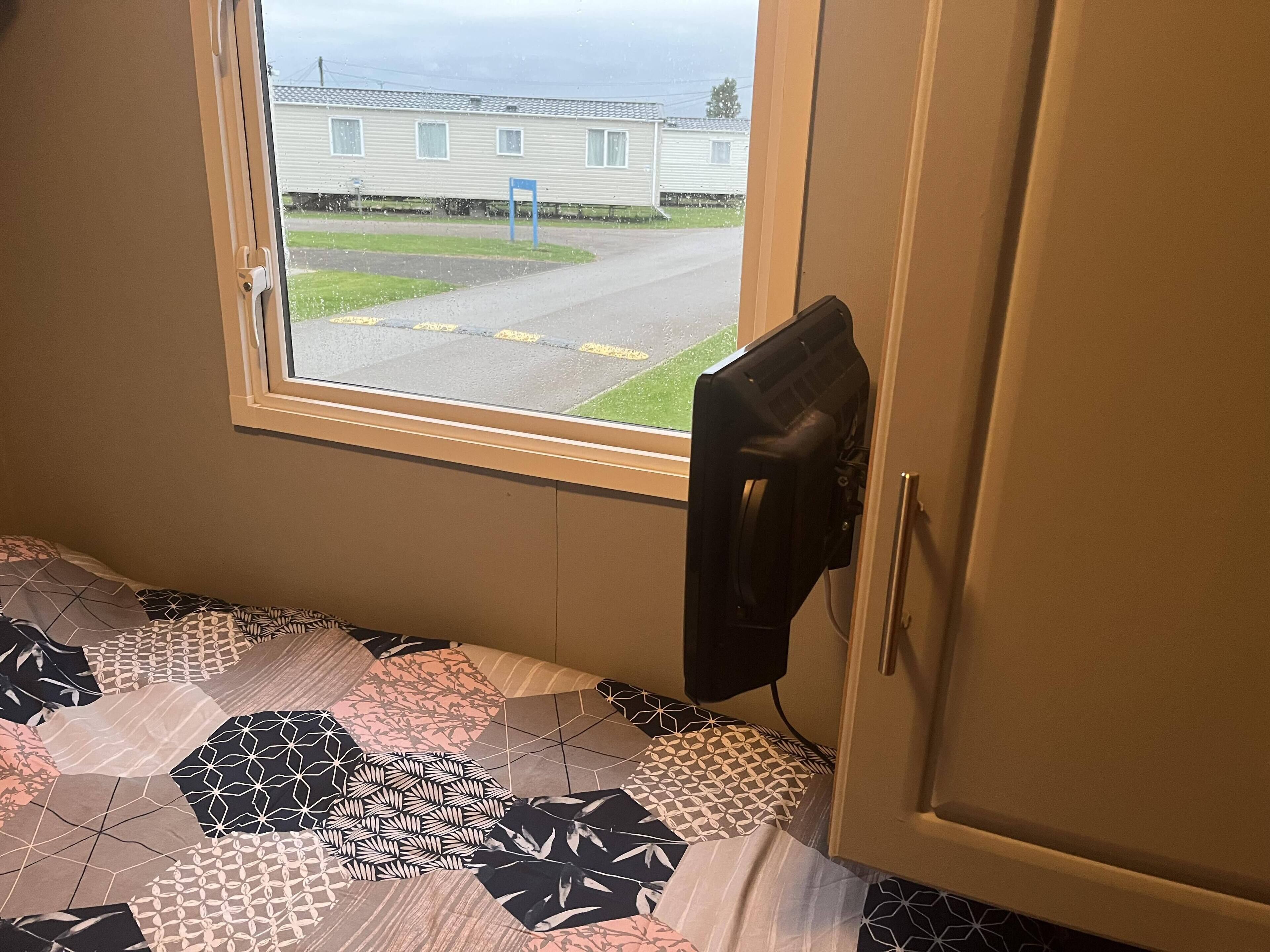 A bedroom with a window, a bed with patterned bedding, and a door with a black object on it.