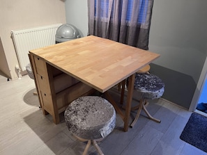 A wooden dining table with two stools, a radiator, and a window with curtains.