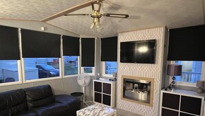 Ein modernes Wohnzimmer mit einem schwarzen Ledersofa, einem weißen Couchtisch, einem Kamin, einem darüber montierten Fernseher und einem Deckenventilator.
