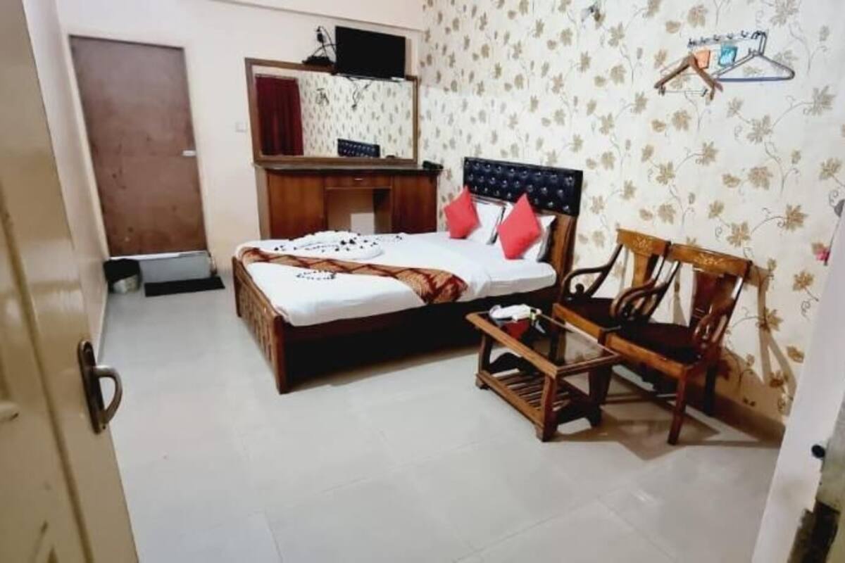 Un dormitorio con cama, una silla de madera, un armario y un televisor en la pared.