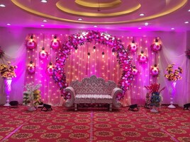 Un escenario con un arco floral y un banco, rodeado de cortinas decorativas y arreglos florales.