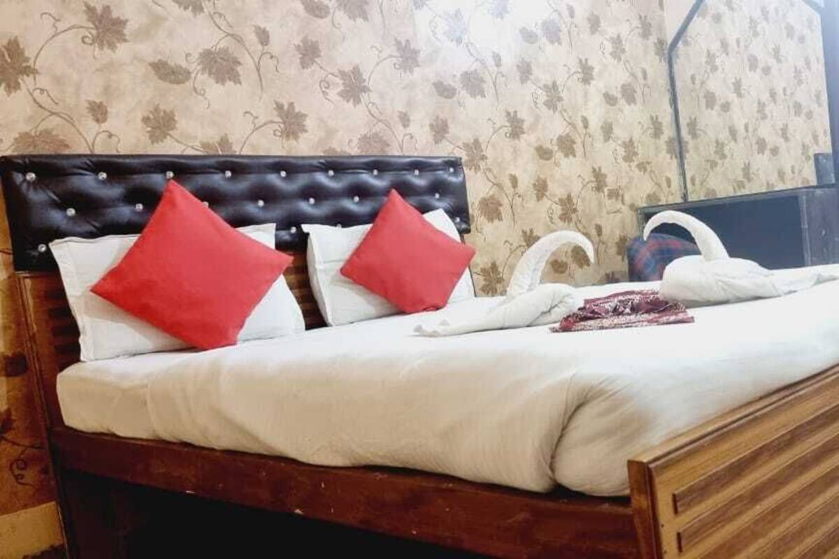 Una cama con estructura de madera y cabecera, con dos almohadas rojas y una blanca.