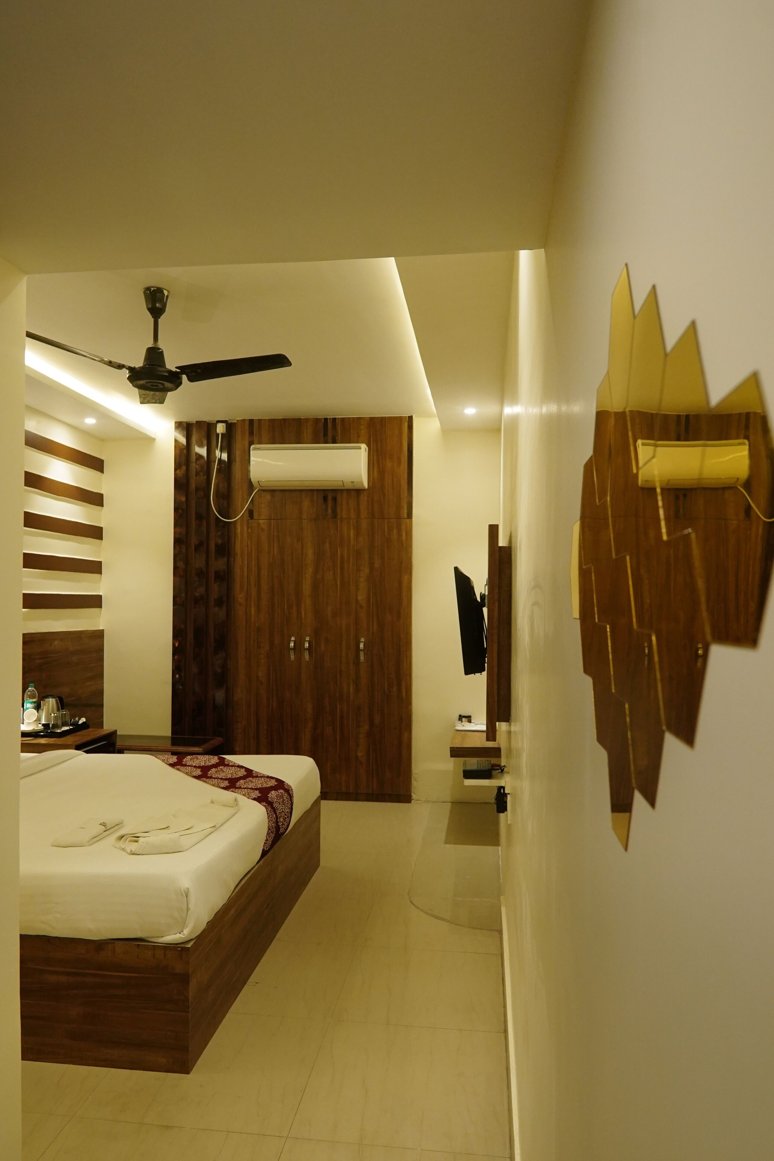 A modern bedroom with a wooden bed, a ceiling fan, an air conditioning unit, and a wall-mounted TV.