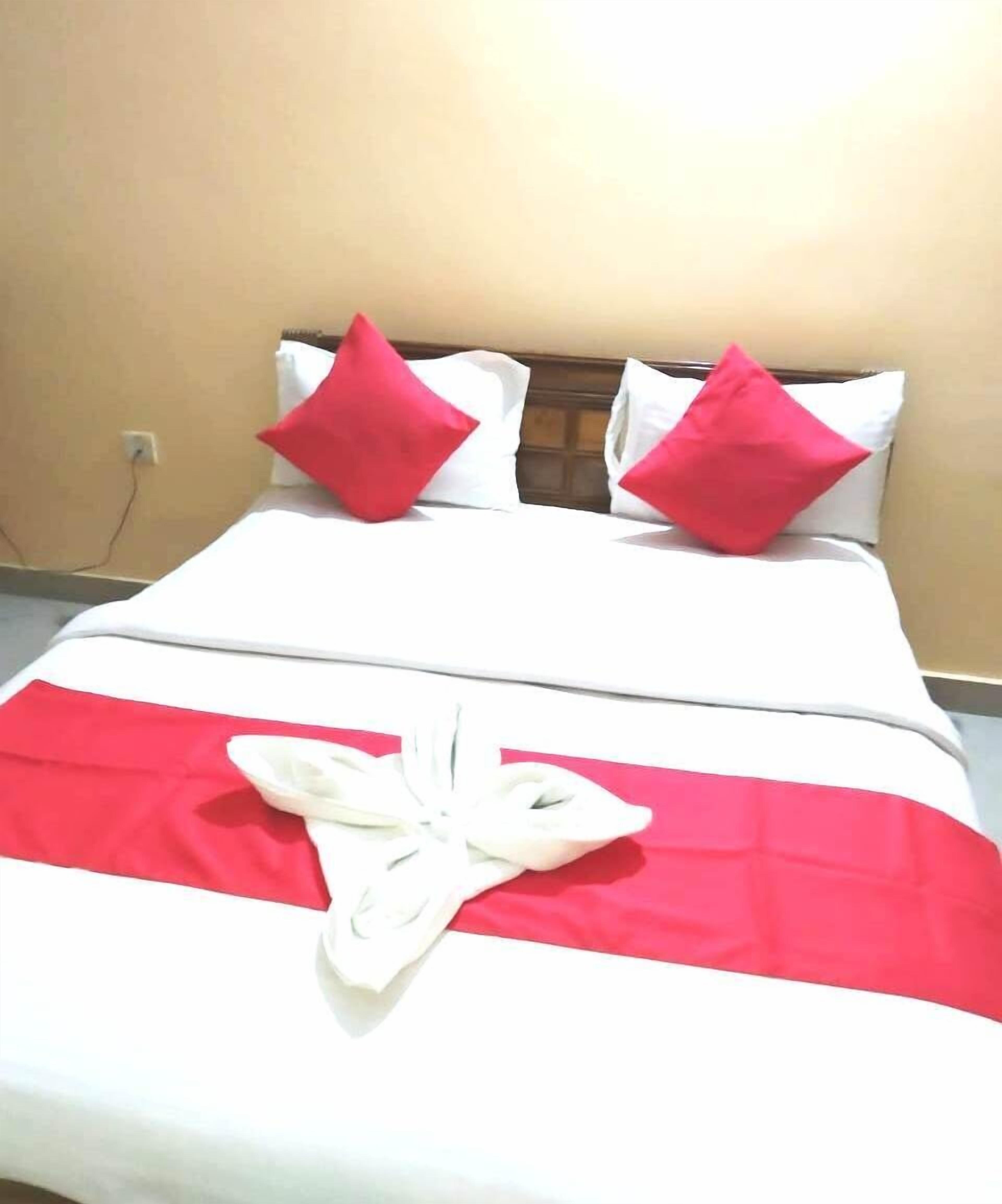 Una cama con ropa de cama blanca y roja, dos almohadas rojas y una toalla blanca.