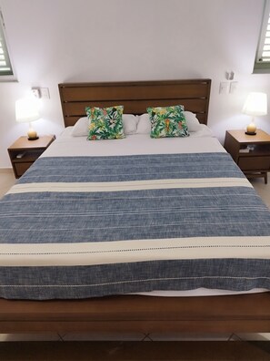 Un lit avec une couvre-lit à rayures, deux oreillers assortis, une tête de lit en bois, deux tables de chevet avec des lampes et un mur blanc.