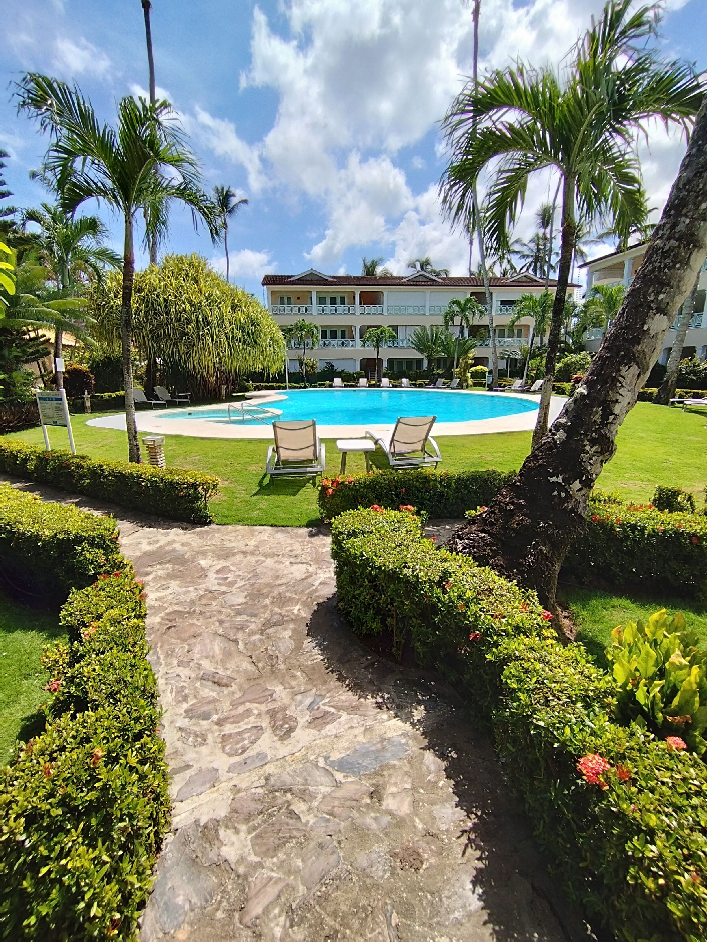 A pool area with lounge chairs, a stone pathway, and a building in the background.