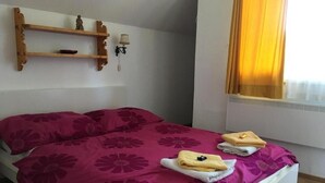 A bed with a floral bedspread, two towels, a shelf with decorative items, and a window with curtains. - Cozy and centrally located vacation home 500 meters from the cable car/ski slope (Mitterstoder)