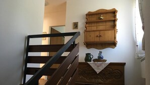 A wooden staircase with a black handrail leading to a landing. A wooden cabinet with a decorative top is mounted on the wall above a small table with a cloth. - Cozy and centrally located vacation home 500 meters from the cable car/ski slope (Mitterstoder)