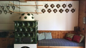 A cozy cabin interior with a wooden bed, a green stove, and wall-mounted decorations. - Cozy and centrally located vacation home 500 meters from the cable car/ski slope (Mitterstoder)