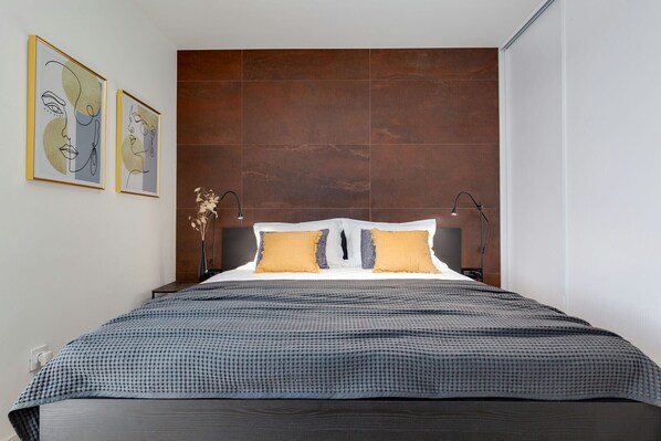 Un dormitorio moderno con una cama grande, dos mesitas de noche, un cabecero y dos cuadros abstractos en la pared.