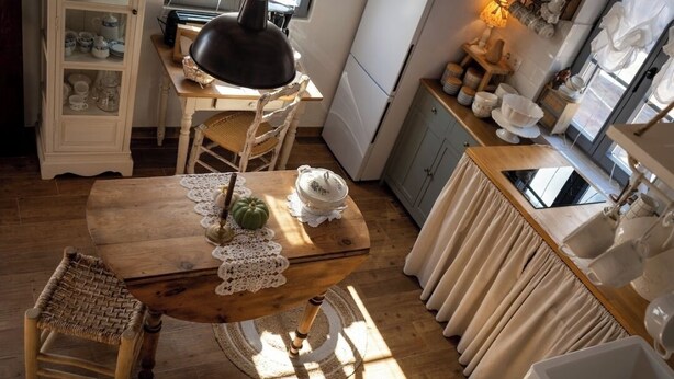 A cozy kitchen with a wooden table, wicker chair, and a cabinet filled with dishes. - Rural cottage in Riocorvo (riocorvo)