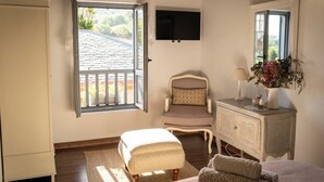 A bedroom with a large window, a chair, a bedside table with a lamp, and a TV mounted on the wall. - Rural cottage in Riocorvo (riocorvo)