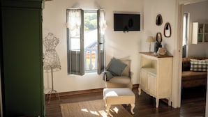 A cozy room with a wooden floor, a green cabinet, a wicker chair, a white bench, and a small table with a lamp. - Rural cottage in Riocorvo (riocorvo)