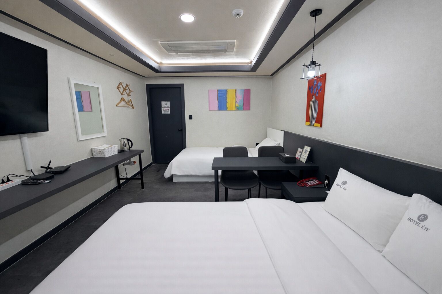 A hotel room with two beds, a desk, a TV, and a door.