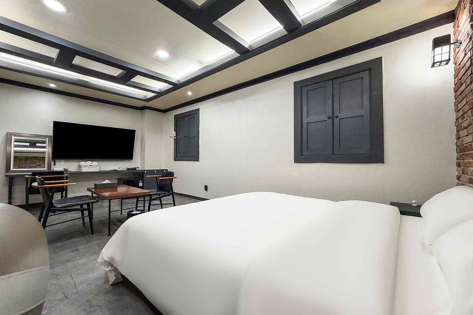 A hotel room with a bed, a desk, a chair, and a TV.