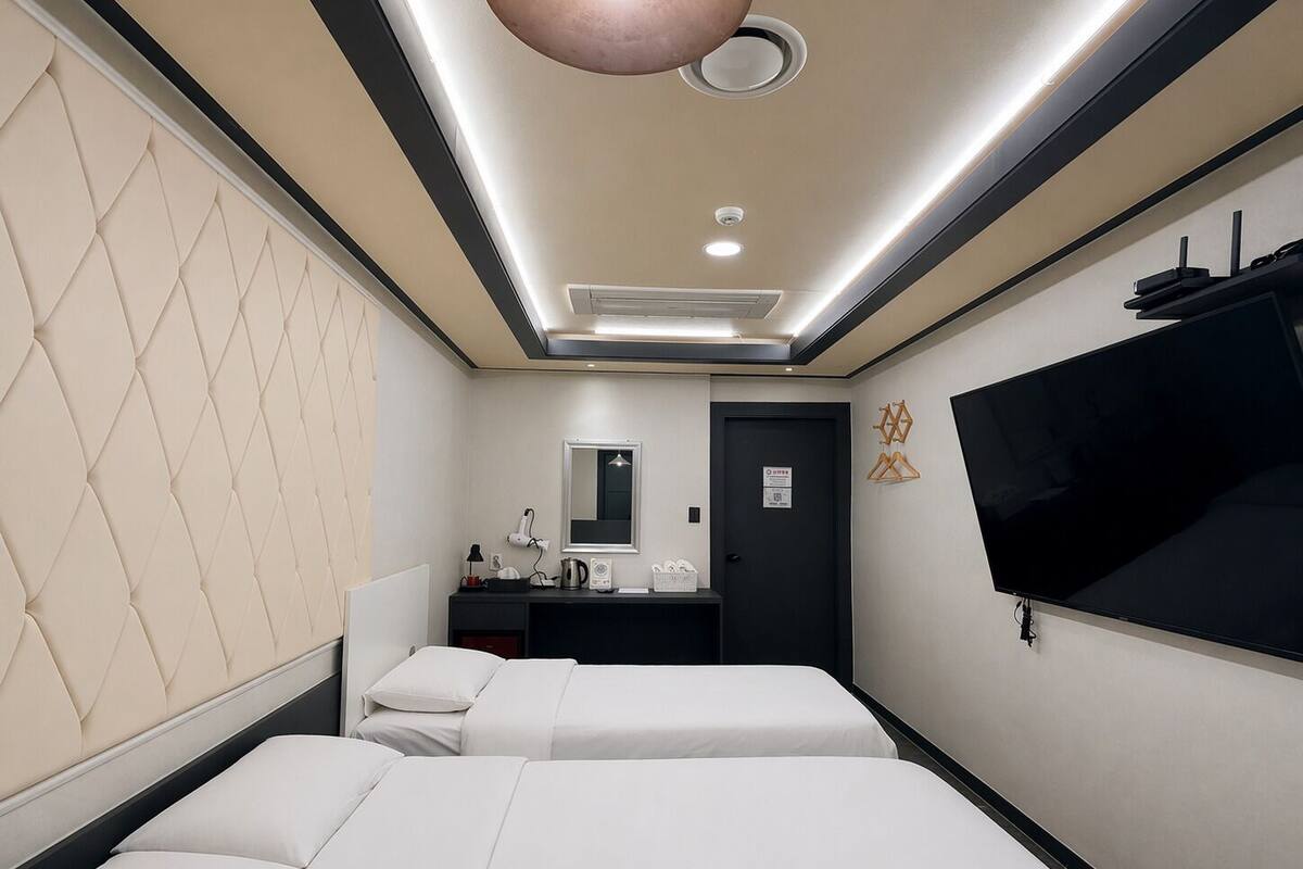 A hotel room with two beds, a vanity with a mirror, a flat-screen TV, and a ceiling light fixture.