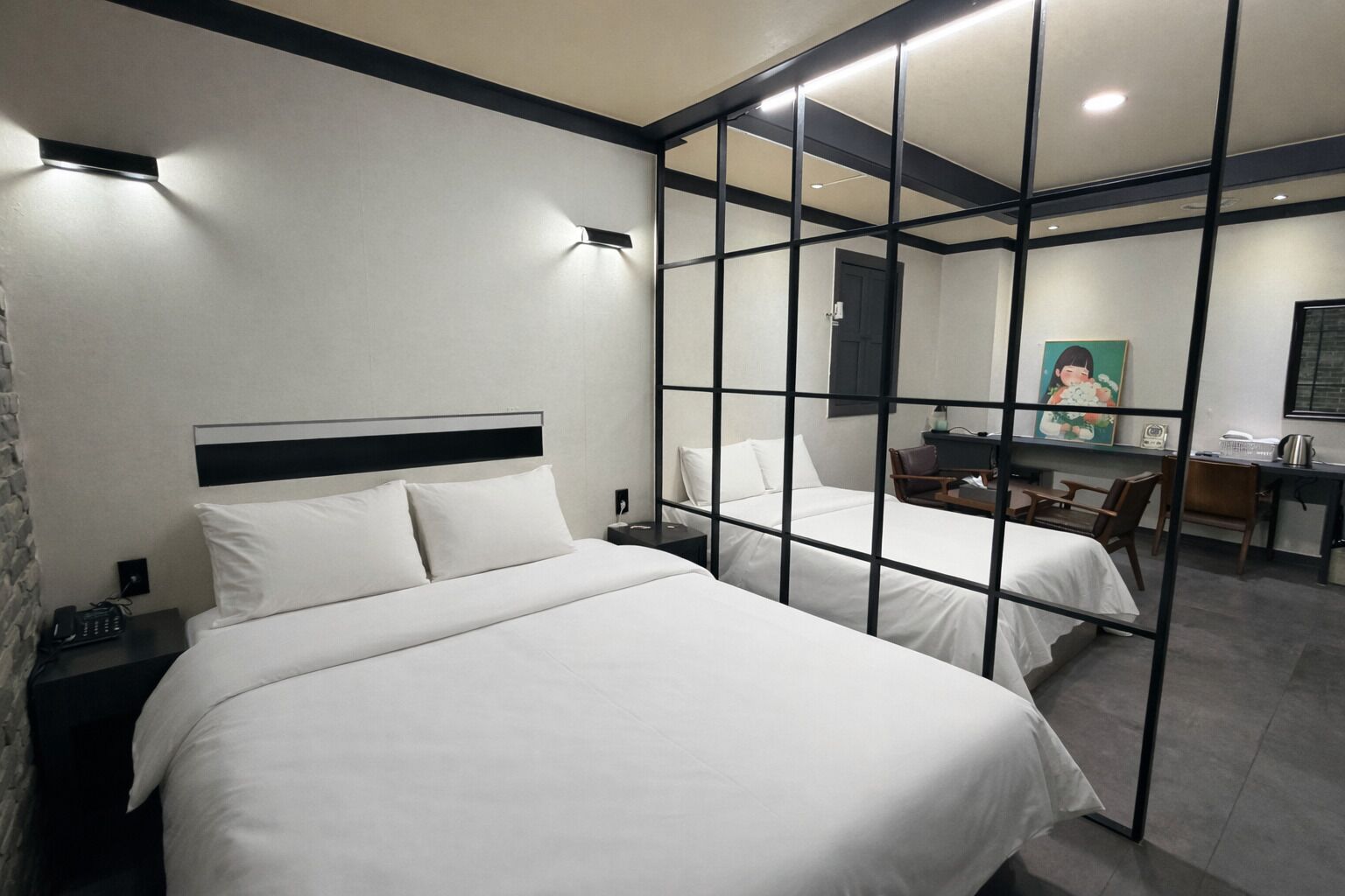 A hotel room with two beds, a desk, a chair, a small table, and a mirror.