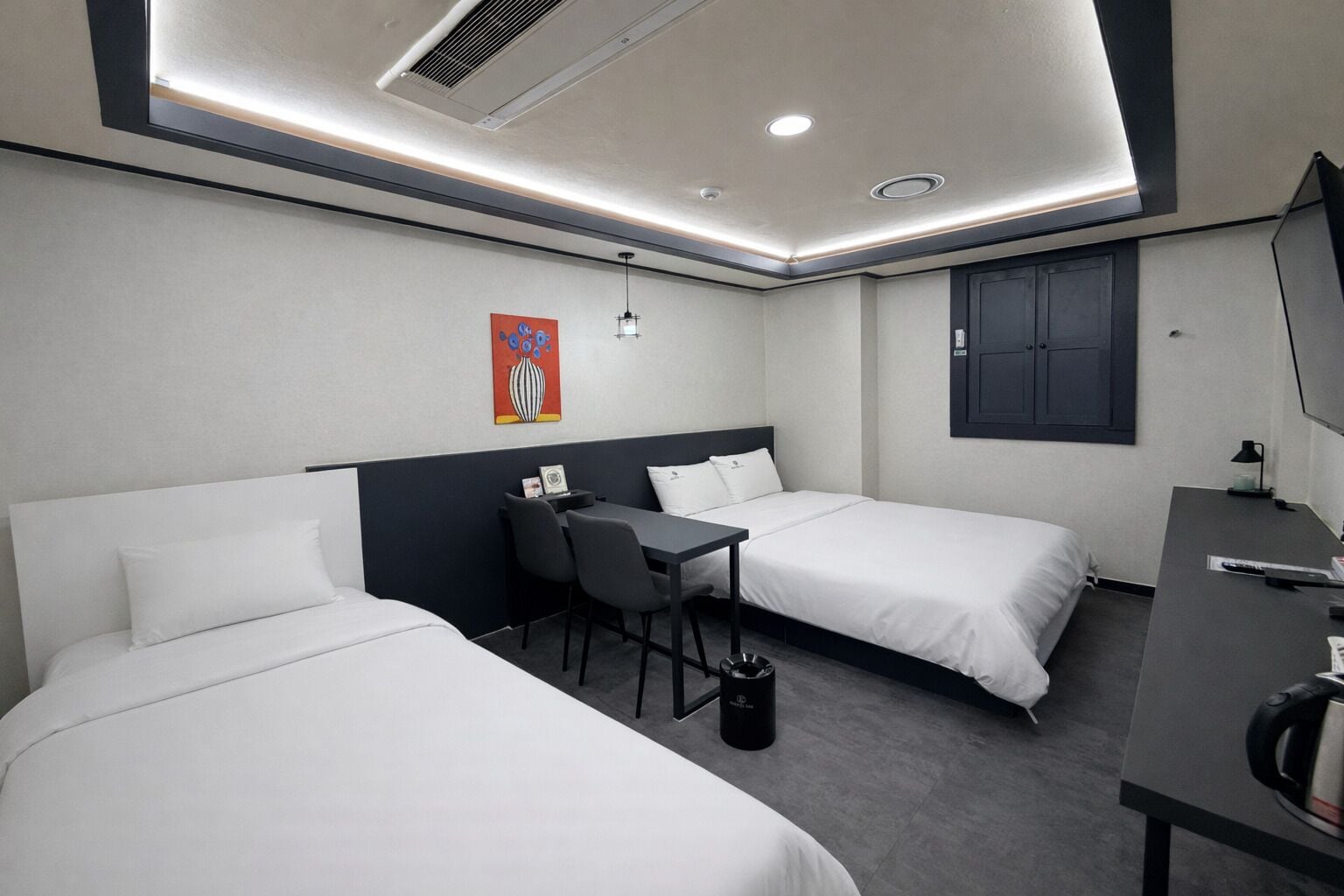 A hotel room with two beds, a desk, a chair, a trash bin, and a painting on the wall.