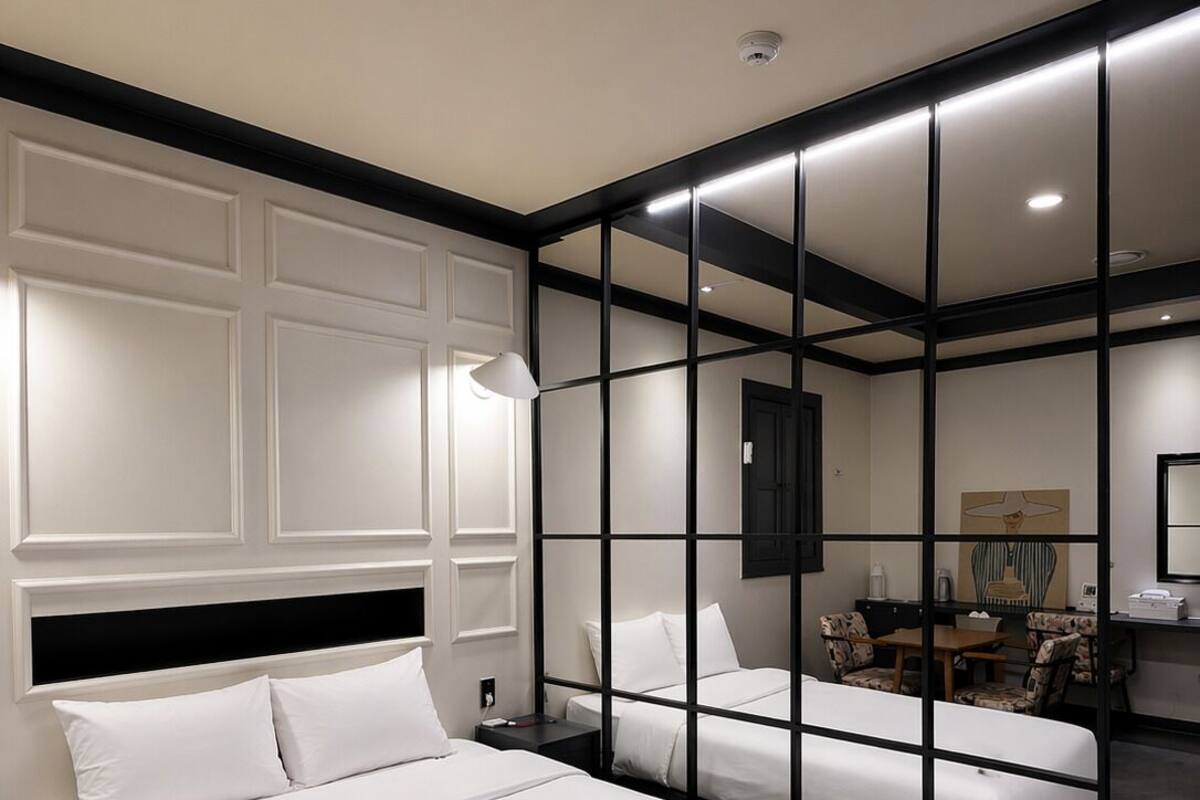 A modern hotel room with two beds, a desk, a chair, and a large mirror.