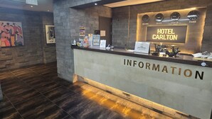 A hotel reception desk with a modern design, featuring a clock displaying multiple time zones, a sign reading "HOTEL CARLTON," and a "INFORMATION" sign. - Hotel Carlton Incheon Airport Juan (Incheon)