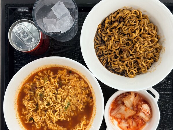 A tray with two bowls of instant noodles, one with a spicy broth and the other with a clear broth, and a small bowl of kimchi. - Hotel Carlton Incheon Airport Juan (Incheon)