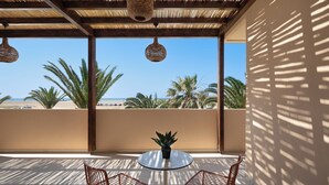 Een balkon met twee stoelen, een klein tafeltje en een bloempot. Het balkon heeft uitzicht op een strand met palmbomen en de oceaan.