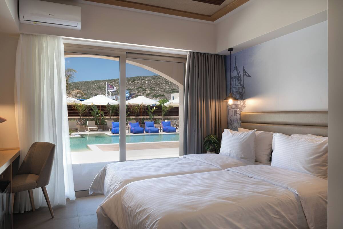 Ein Hotelzimmer mit einem großen Bett, einem Schreibtisch und Blick auf einen Poolbereich mit Liegestühlen.