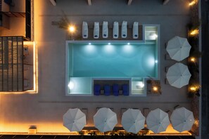 A rooftop pool area with a rectangular pool, lounge chairs, umbrellas, and a seating area with blue cushions. - Prasonisi Light House Boutique Hotel (Rhodes)
