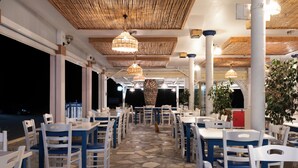 Een buiten eethoek met witte en blauwe tafels en stoelen, stenen vloeren en hangende rieten lampen.