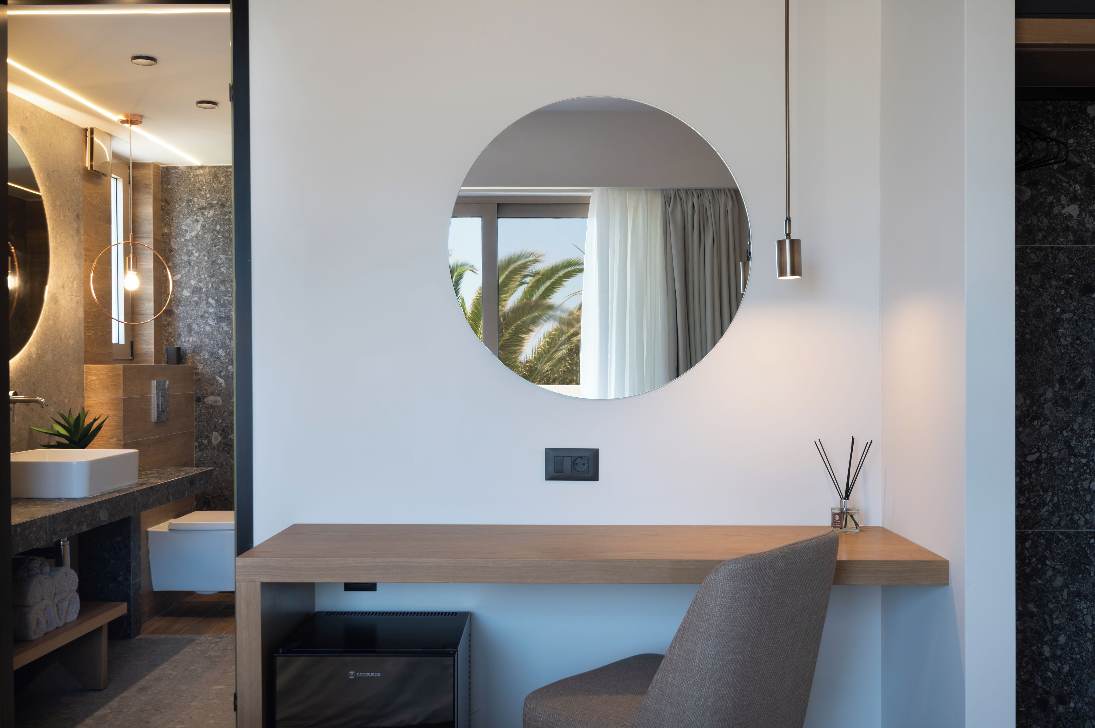 A modern bathroom with a round mirror, a sink, and a toilet.