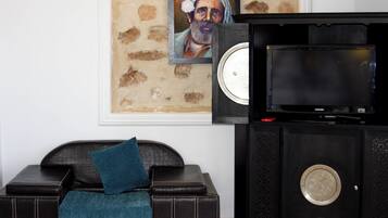 A room with a black entertainment unit, a framed artwork on the wall, a dark leather sofa with a teal pillow, and a television.