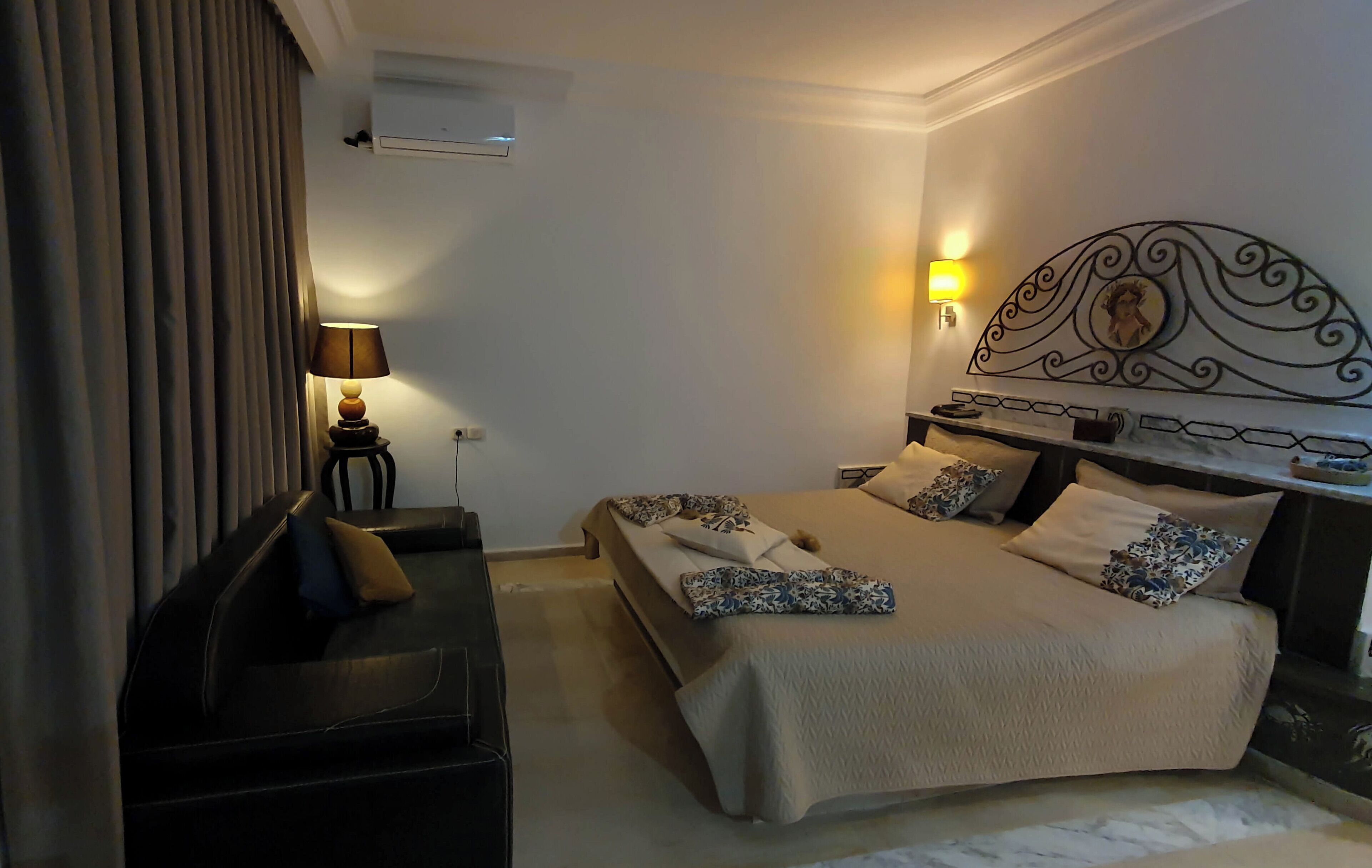 A hotel room with a bed, bedside table, lamp, and curtains.