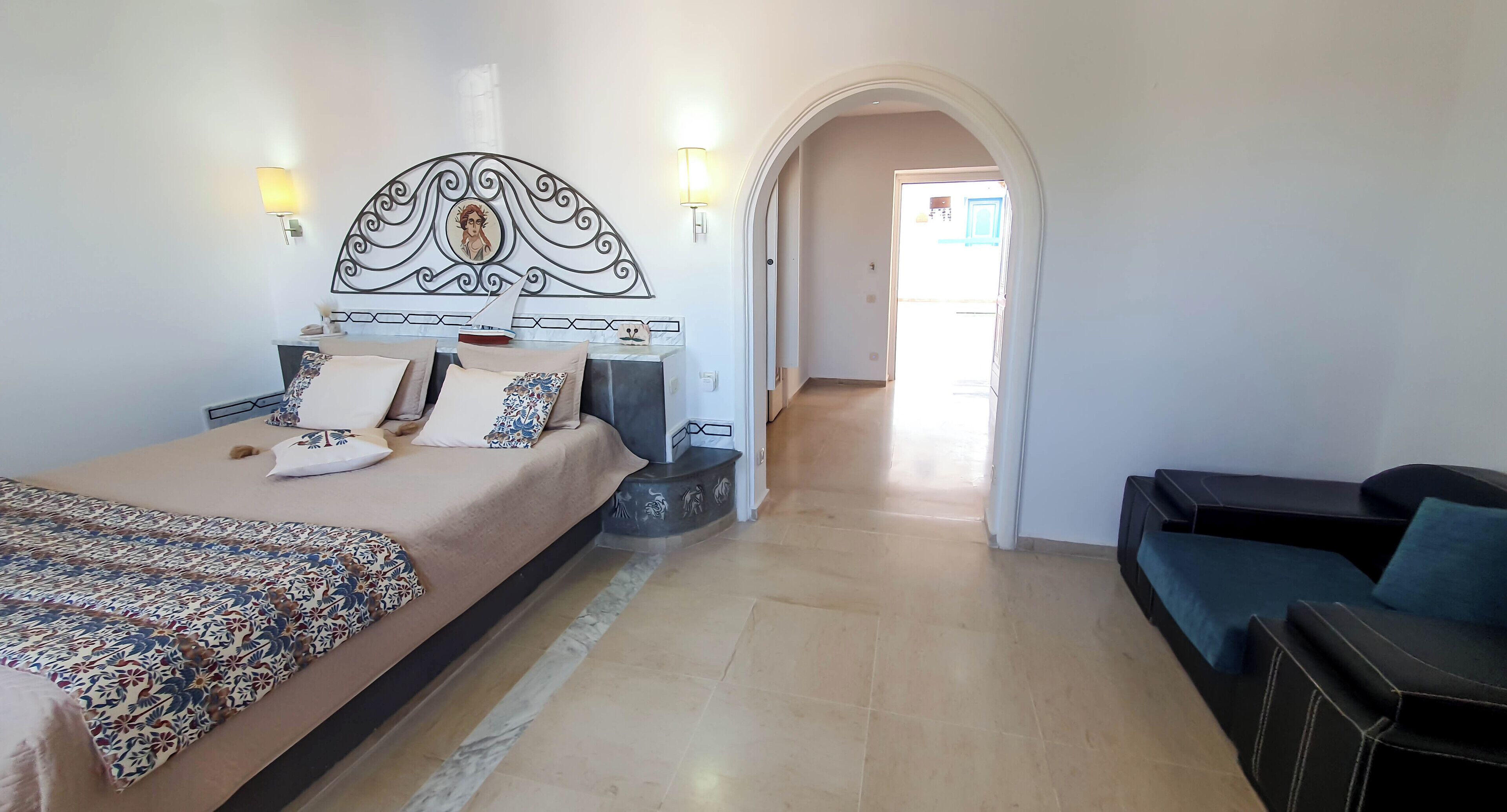 A bedroom with a bed, a sofa, a decorative headboard, and a hallway leading to another room.